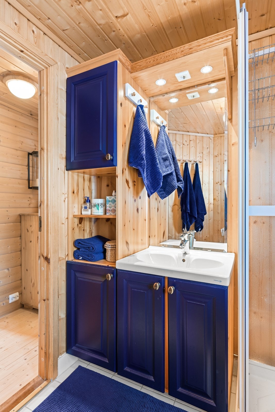 Det er fliser på gulv med varmekabler under. Dusjkabinett, vask i seksjon, speil med belysning og toalett. Galleribilde