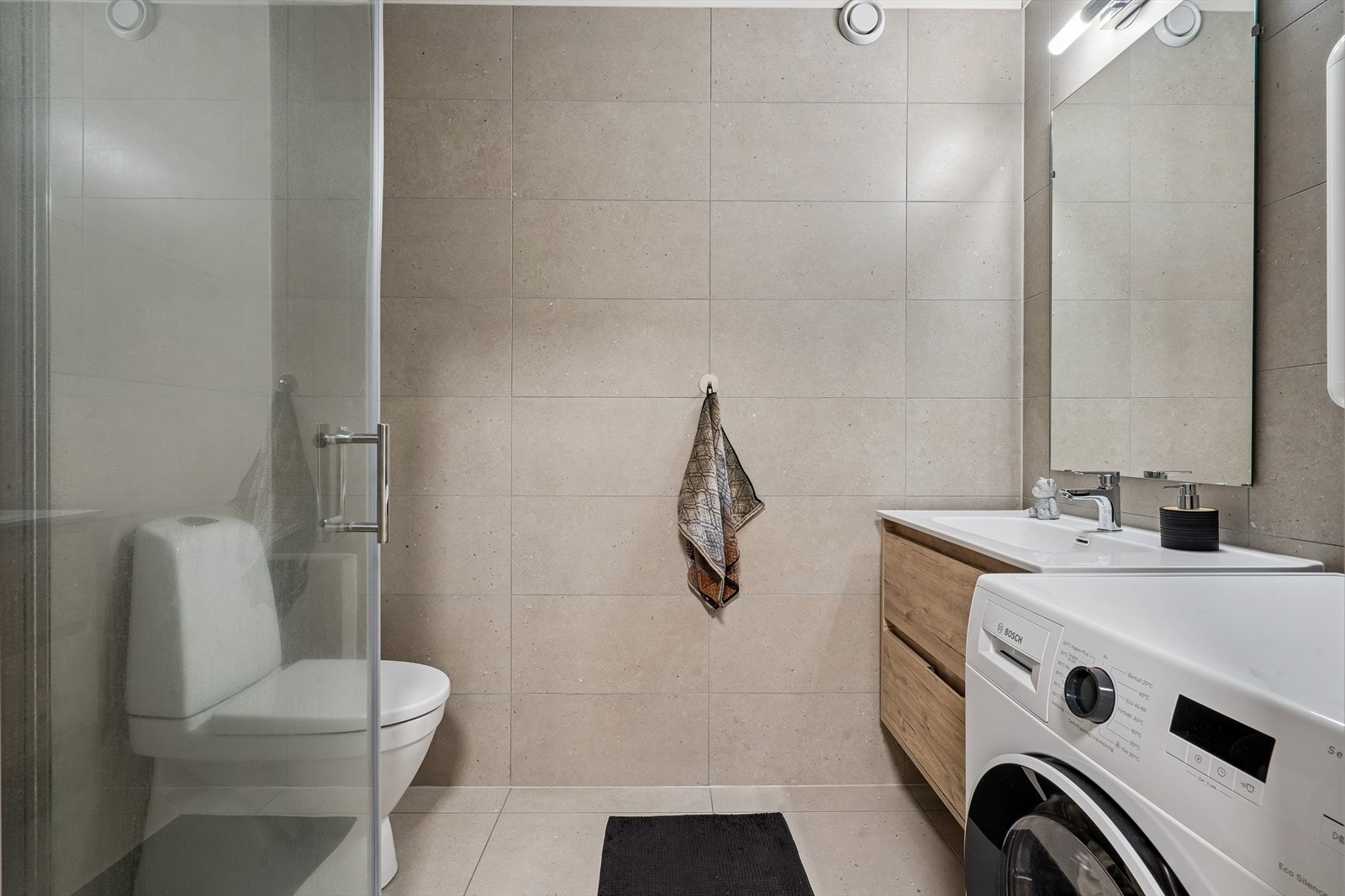 Det delikate badet er utstyrt med dusjhjørne med glassdører, gulvstående toalett og opplegg for vaskemaskin. Galleribilde