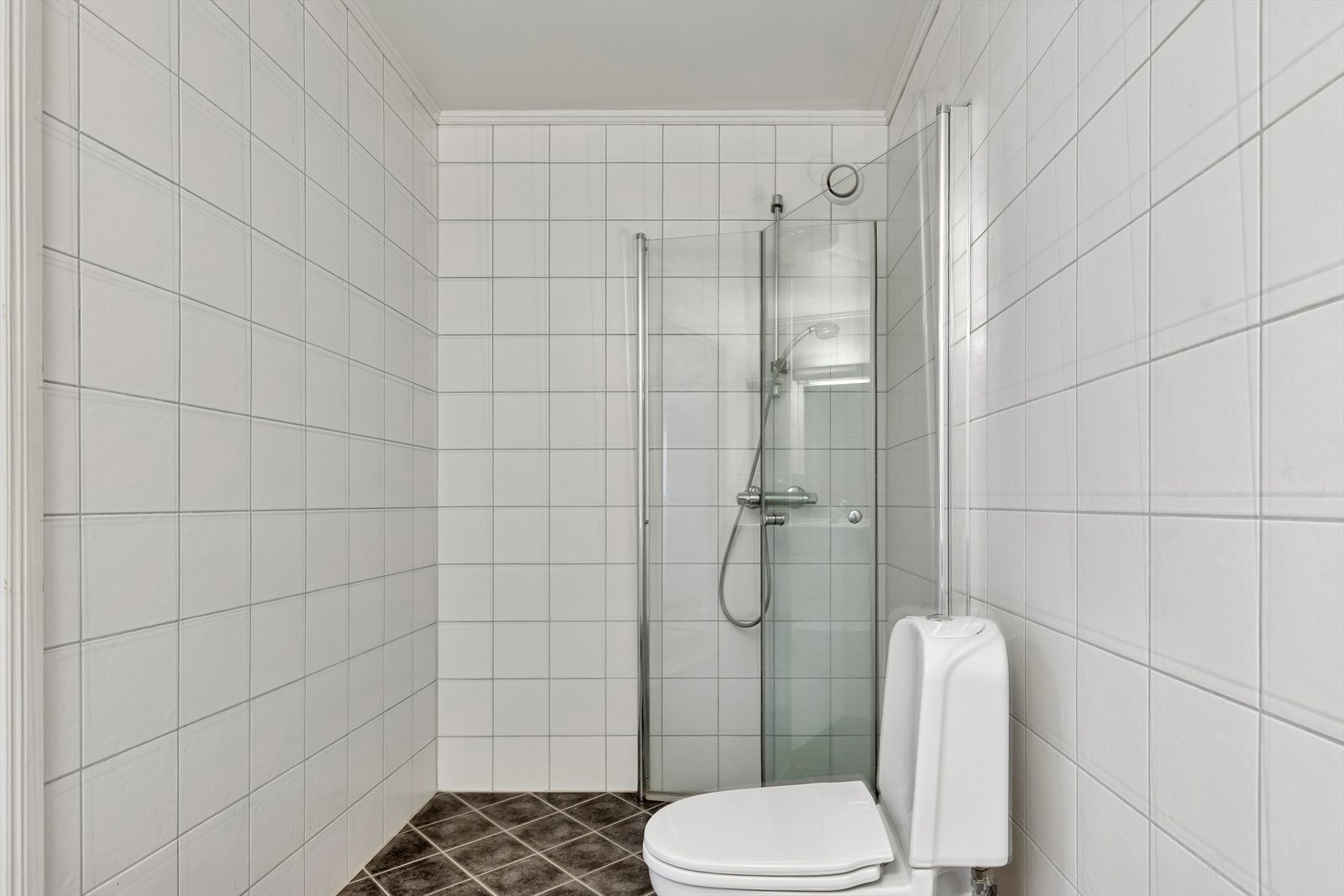 Badet er flislagt og praktisk dusjhjørne med innfellbare dører i glass. Galleribilde