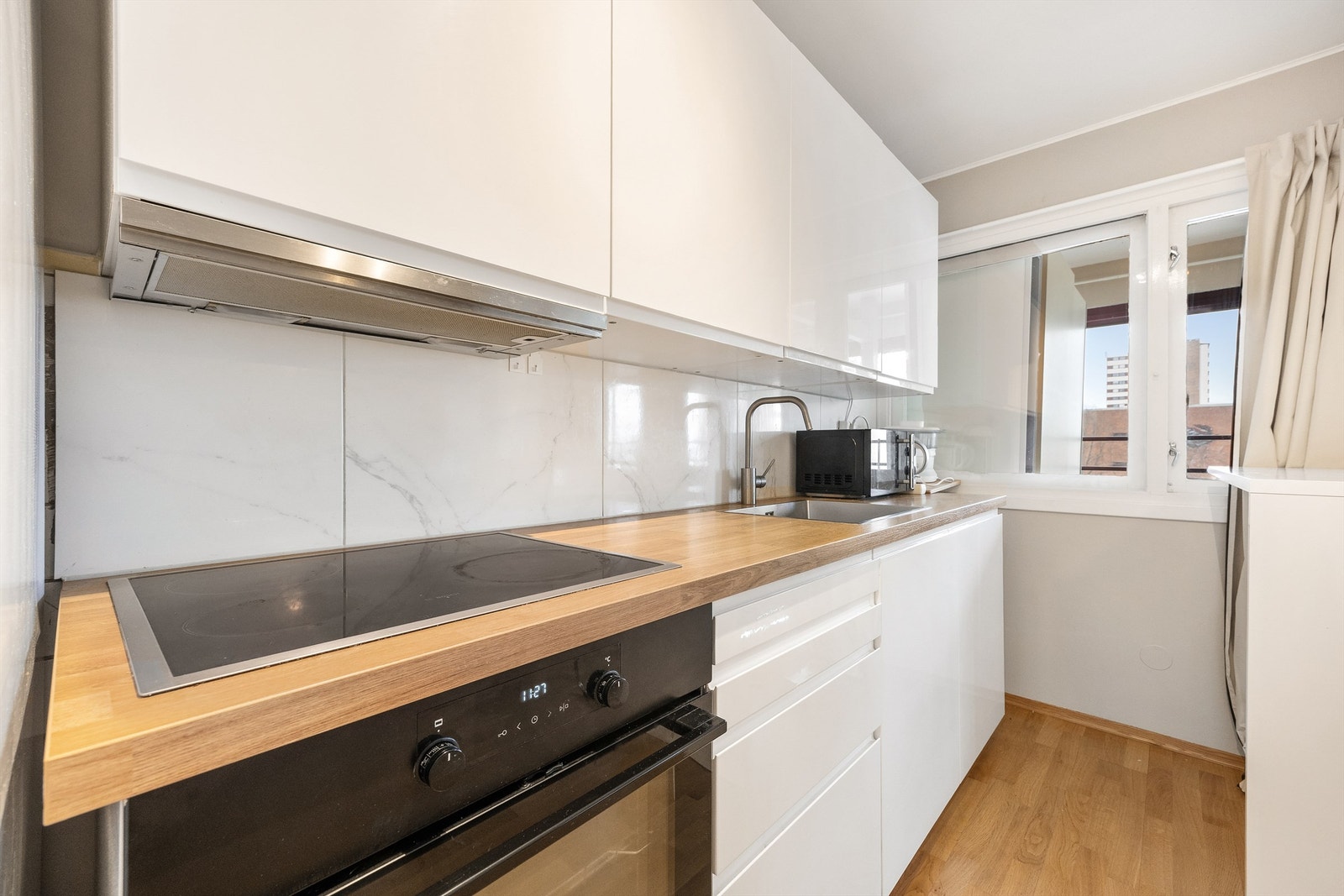 Kjøkkeninnredning av glatte fronter samt fliser mellom overskap og benkeplate Galleribilde