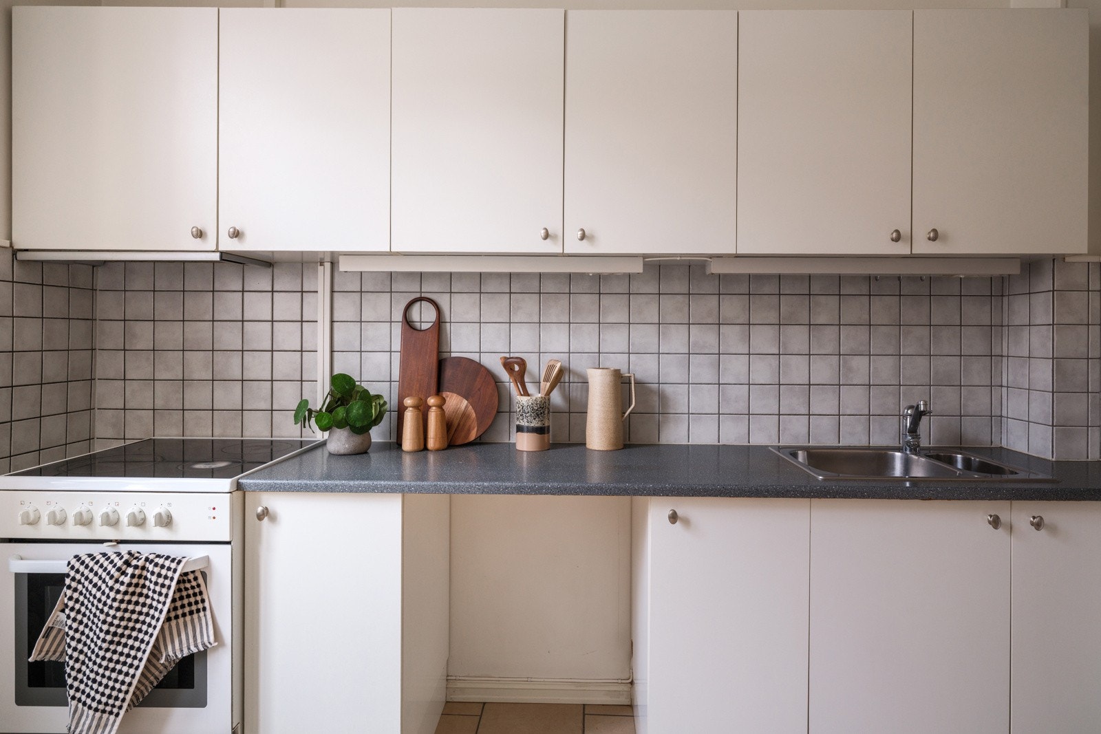 Eldre kjøkkeninnredning med god skap- og benkeplass. Innredningen har hvite glatte fronter og laminert benkeplate med nedfelt oppvaskkum. Praktisk med fliser i benkeryggen og belysning under overskapene. Galleribilde