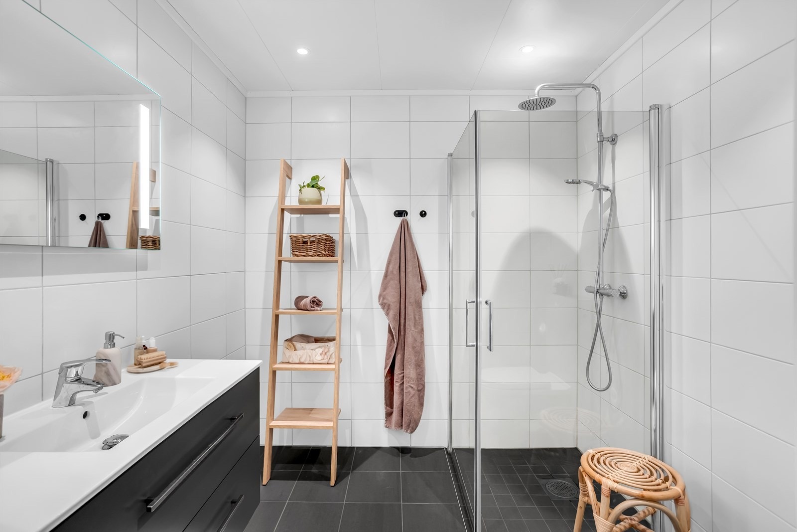 Flislagt baderom med keramiske fliser, nedsenket dusjhjørne med glassdører og finert servantinnredning. Galleribilde