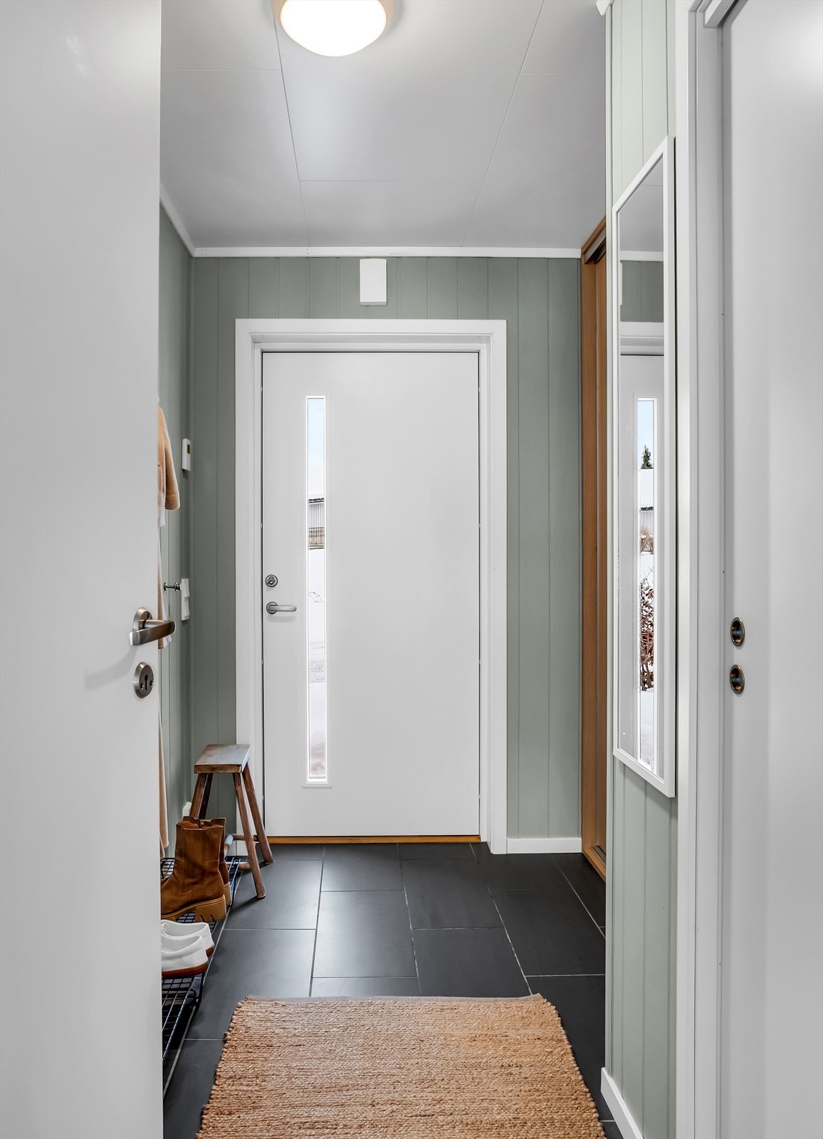 Inngangspartiet har en tidsmessig ytterdør med glassfelt som leder inn til en praktisk gang. Galleribilde
