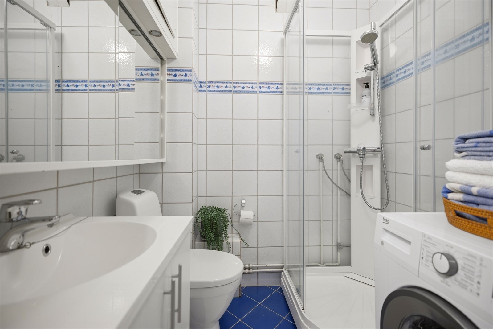 Badet er innredet med toalett, dusjkabinett, servantinnredning og overskap med speilfronter. Opplegg for vaskemaskin. Galleribilde