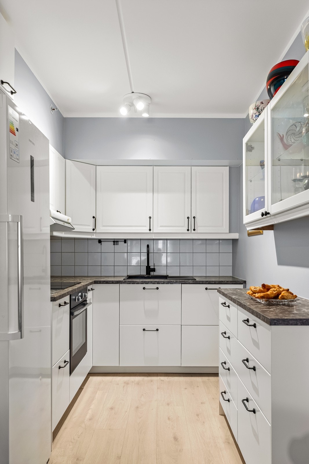 Kjøkkenet har lys innredning med laminat benkeplate i mørk tone.
Praktiske arbeidsflater og funksjonelle løsninger gjør kjøkkenet enkelt å trives i til daglig. Kjøkken er utstyrt med integrert komfyr, platetopp og oppvaskmaskin. Galleribilde