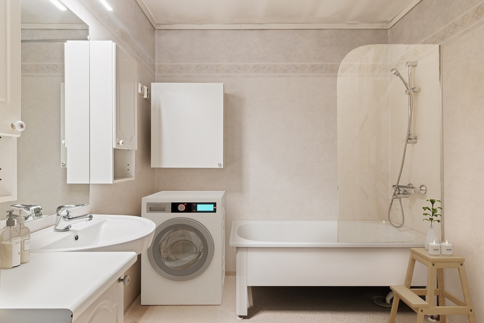 Bad/vaskerom innredet med badekar med dusjstang, servant, speil, veggskap, høyskap, klosett, underskap og opplegg til vaskemaskin. Gulvvarme Galleribilde