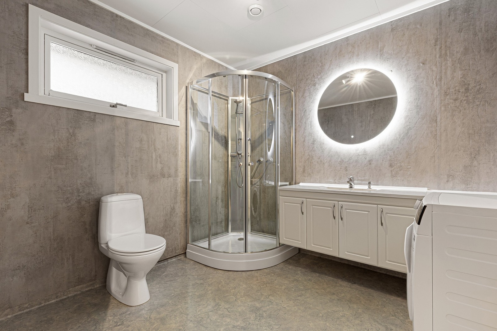 Rommet er innredet med nedfelt servant, toalett, dusjkabinett og opplegg for vaskemaskin. Nytt speil med lys fra 2025. Galleribilde