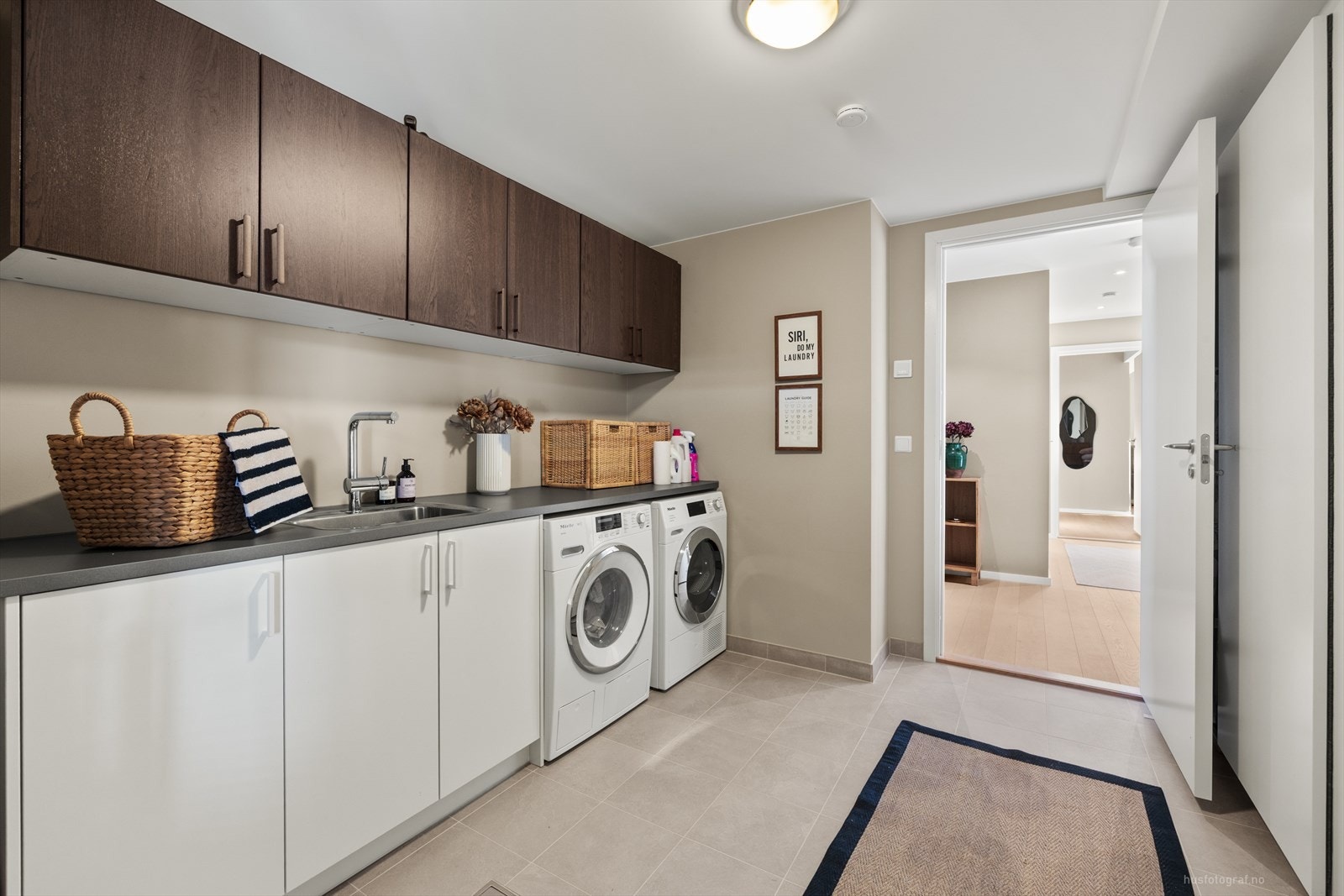 Praktisk og romslig vaskerom med god benkeplass og rikelig oppbevaring i både over- og underskap. Rommet har plass til både vaskemaskin og tørketrommel side om side, samt utslagsvask i innredningen. Galleribilde