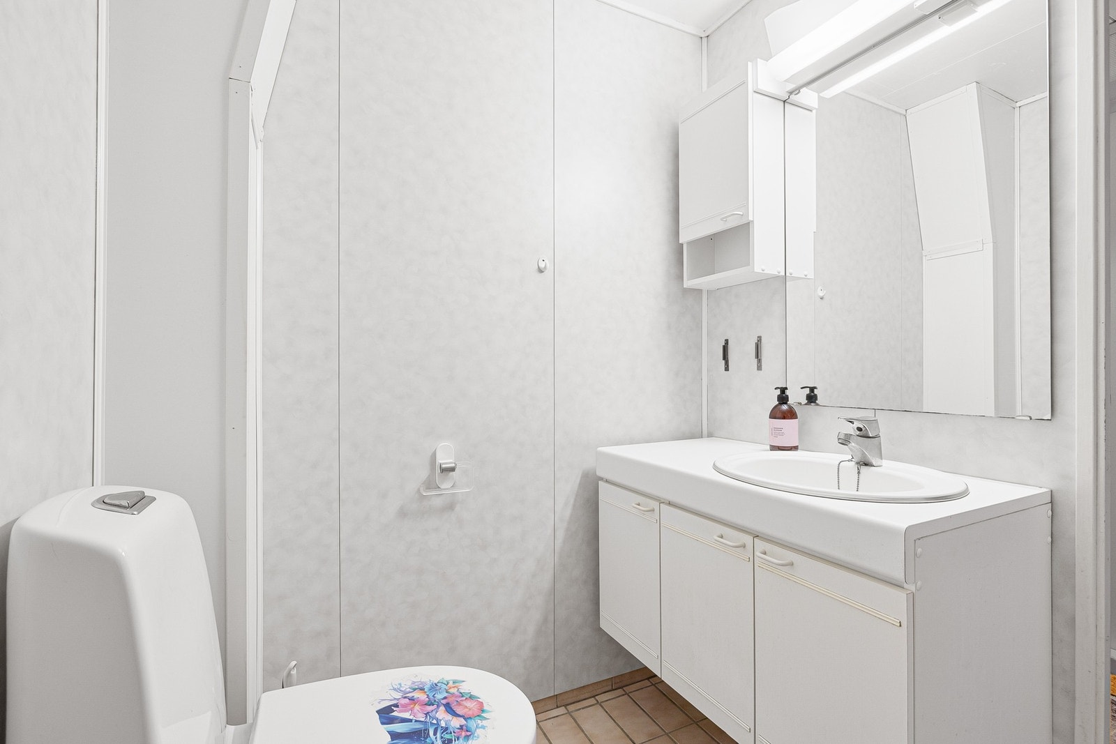 Badet er utstyrt med dusjdører, servantskap, servant og gulmontert toalett. Galleribilde