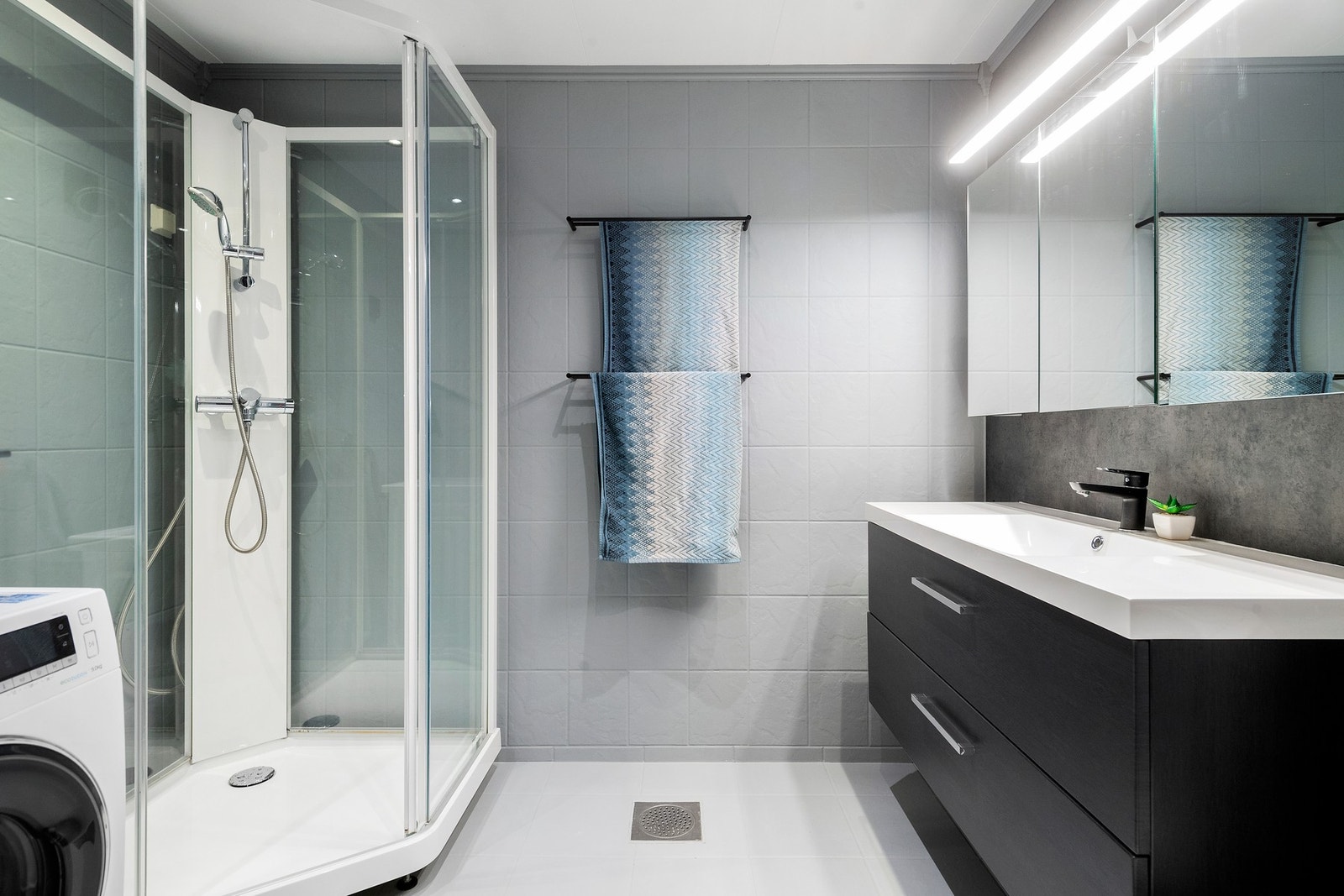 Badet er utstyrt med baderomsinnredning fra 2023 med glatte, mørke fronter og heldekkende servant plate. Av sanitærustyr er det dusjkabinett og gulvmontert toalett. Galleribilde