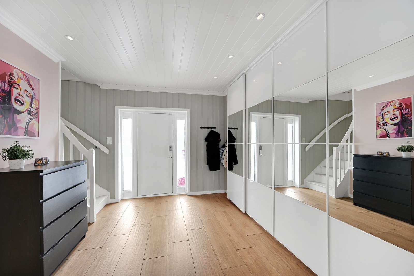 Stor og lekker hall med fliser og varmekabler på gulvet, vegger malt i en moderne farge og lysmalt himling med spott. Det er stor skyvedørsgarderobe med god plass i hallen Galleribilde