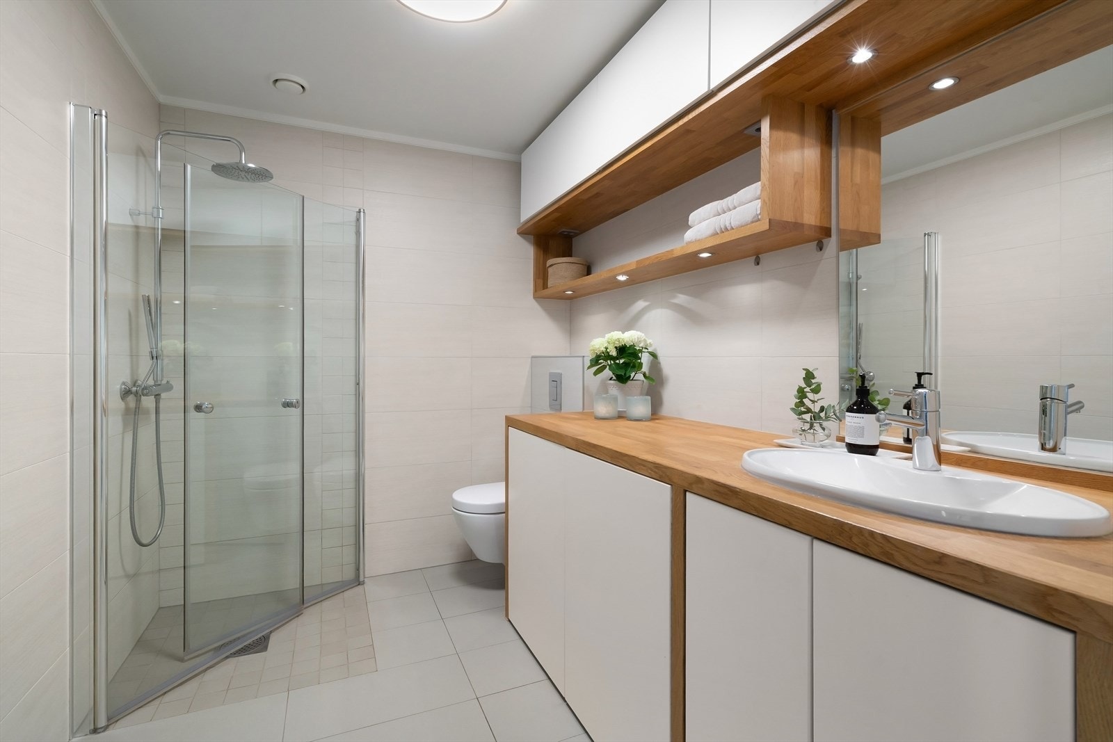 Bad med flis på flis fra 2013. Dusjhjørne med dører i herdet glass, vegghengt toalett og flislagt gulv med varmekabler. Galleribilde