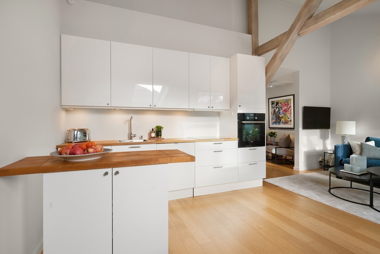 Kjøkken med høyglans glatte fronter, eik benkeplate med nedfelt vaskekum og induksjon platetopp. Nye håndtak til skapfronter fra 2025. Galleribilde