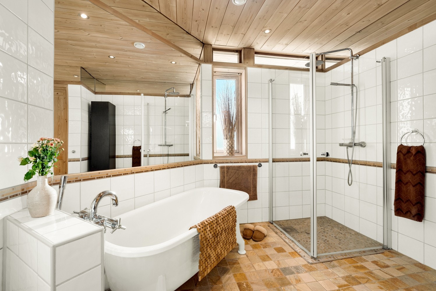 Romslig baderom med både dusj og frittstående badekar, gjennomført med varme naturmaterialer og elegant treverk i himlingen. Naturlig dagslys gjennom vinduene. Galleribilde
