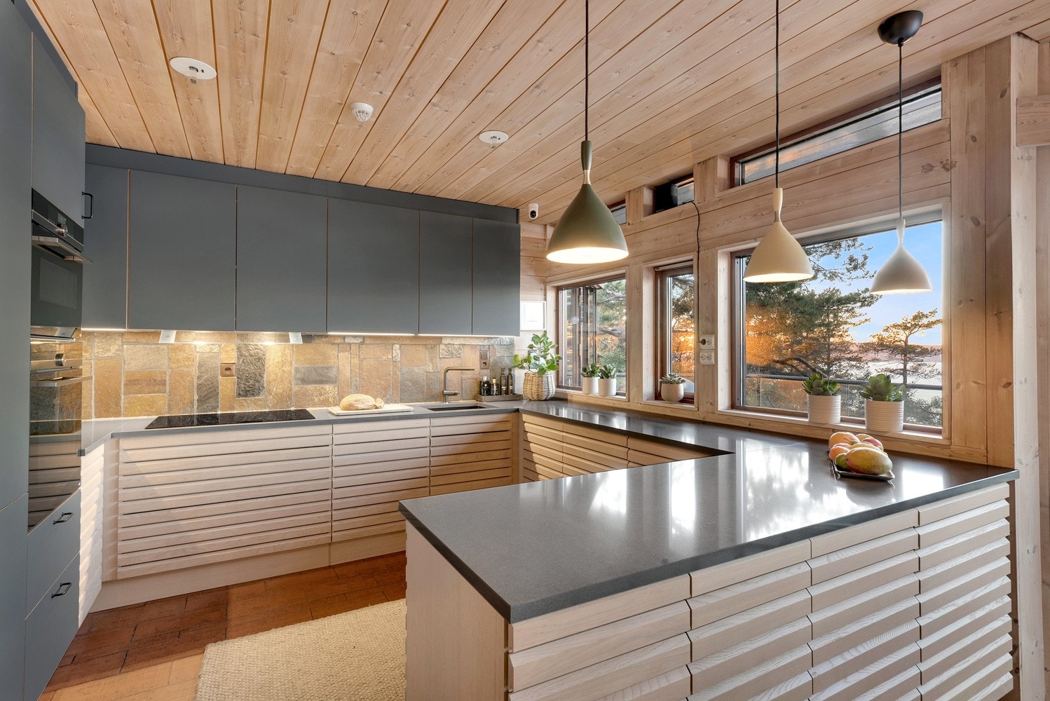 Lekkert HTH-kjøkken fra 2019. Underskapene er bygget i nordisk stil med naturlig, massiv eik. Overskap med slette fronter i en dyp gråtone. Galleribilde