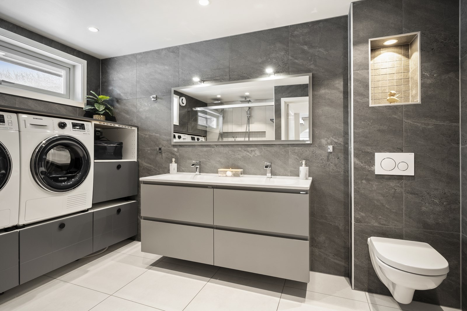 Badet er av god størrelse med flislagte overflater, dobbel servant og egen nisje for vaskemaskin og tørketrommel. Galleribilde