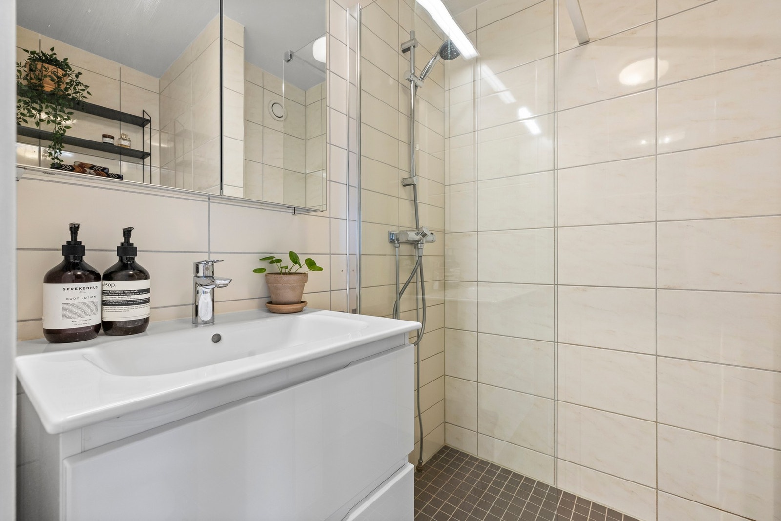 Delikat, flislagt bad med gulvvarme og innredning med nedfelt servant i innredning med skuffer, veggmontert toalett, dusj og opplegg for vaskemaskin. Galleribilde