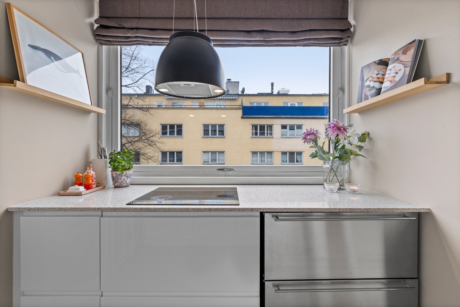 Integrerte hvitevarer som kjøle- og fryseskuff, oppvaskmaskin, induksjonstopp og stekeovn. Fritthengende kjøkken ventilator i sort stål med kullfilter hengende i vaiere fra tak. Galleribilde