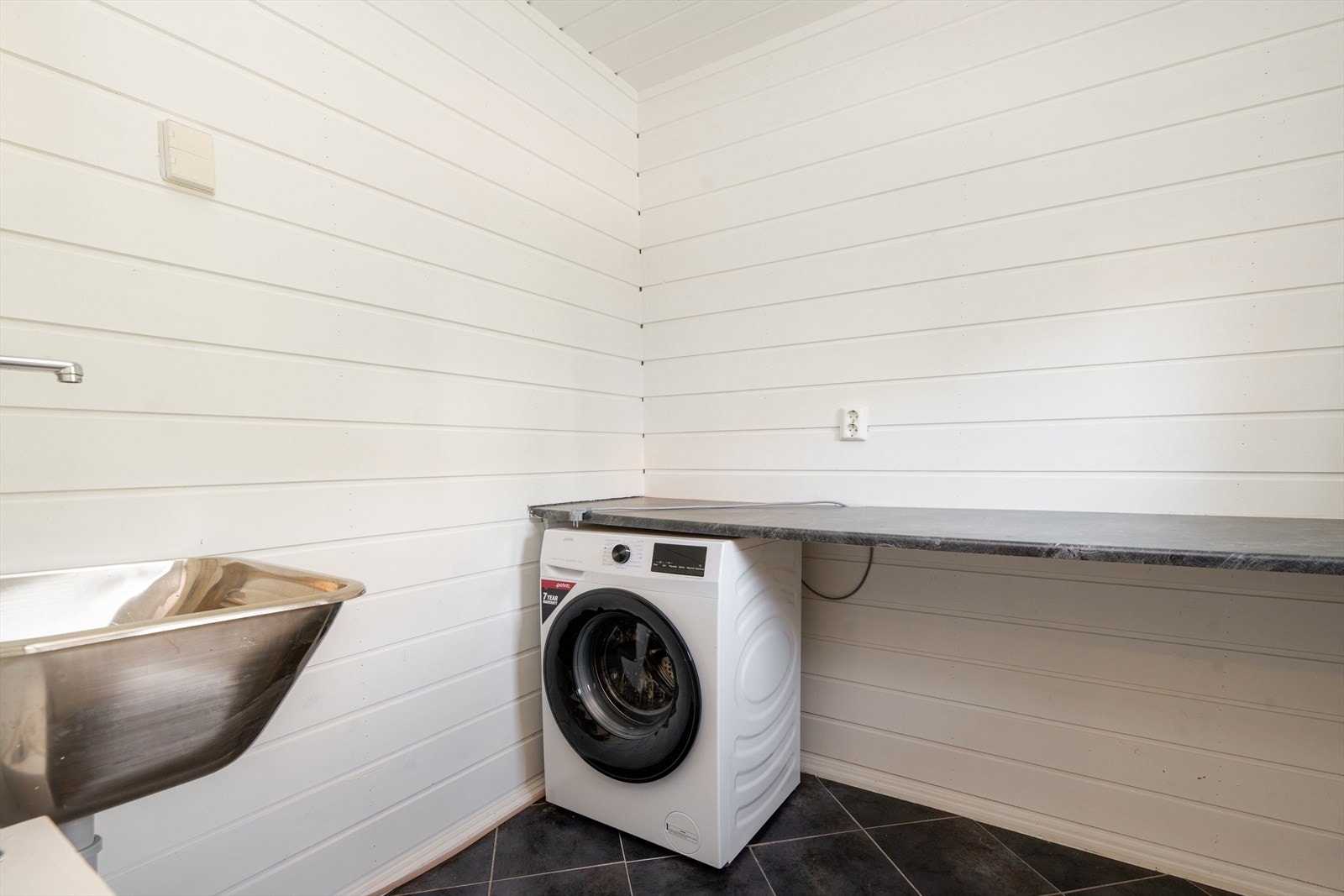 Inntil badet er det etablert et praktisk vaskerom som er innredet med benkeplate og skyllekum. Det er ikke etablert vanntilførsel eller
avløp ved vaskemaskinen. Overflater på vaskerommet er flis på gulv og panel på veggene. Galleribilde