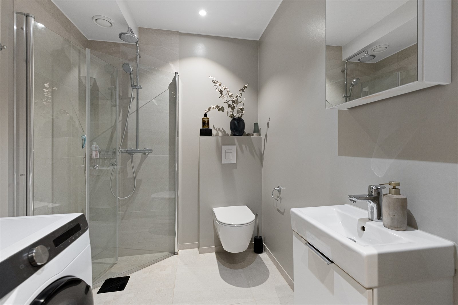 Servantskap med glatte, folierte fronter og speilskap på vegg. Opplegg for vaskemaskin.Dusjhjørne med svingdører, sluk i sone og regnsfalldusj. Galleribilde