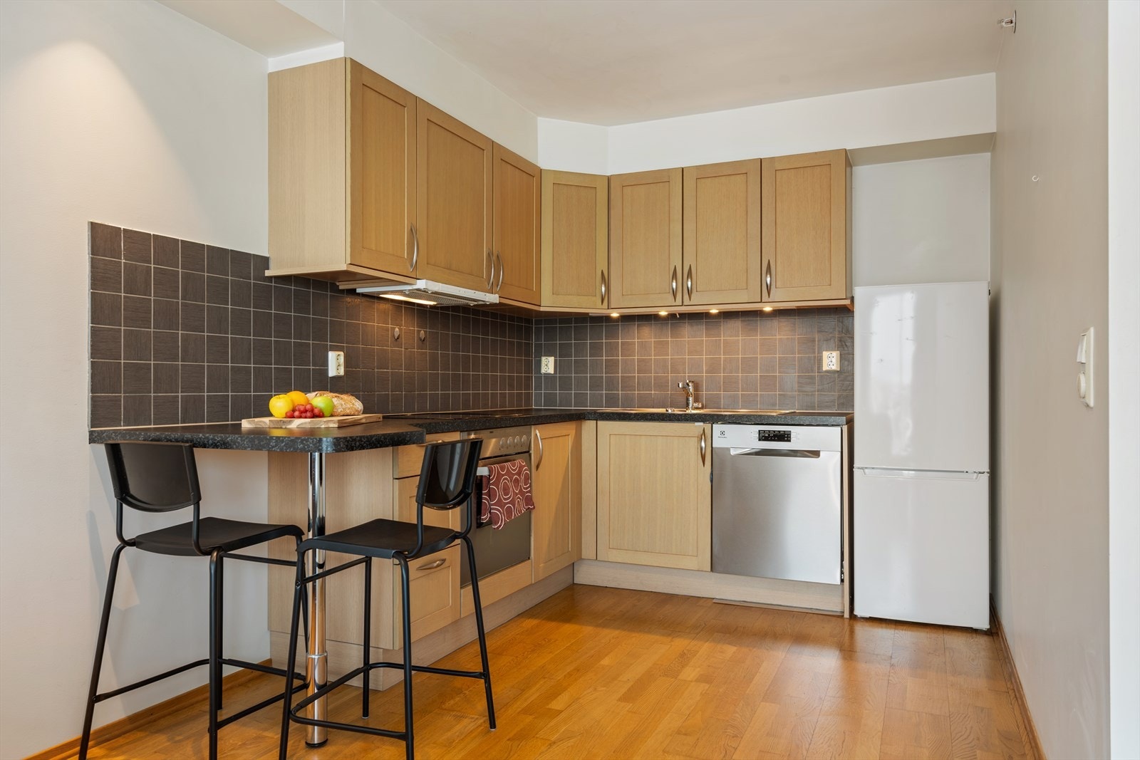 Pen kjøkkeninnredning med profilerte fronter. Laminat benkeplate med vaskebeslag i stål. Stekeovn, platetopp og oppvaskmaskin er integrert i kjøkkenet og medfølger. Galleribilde