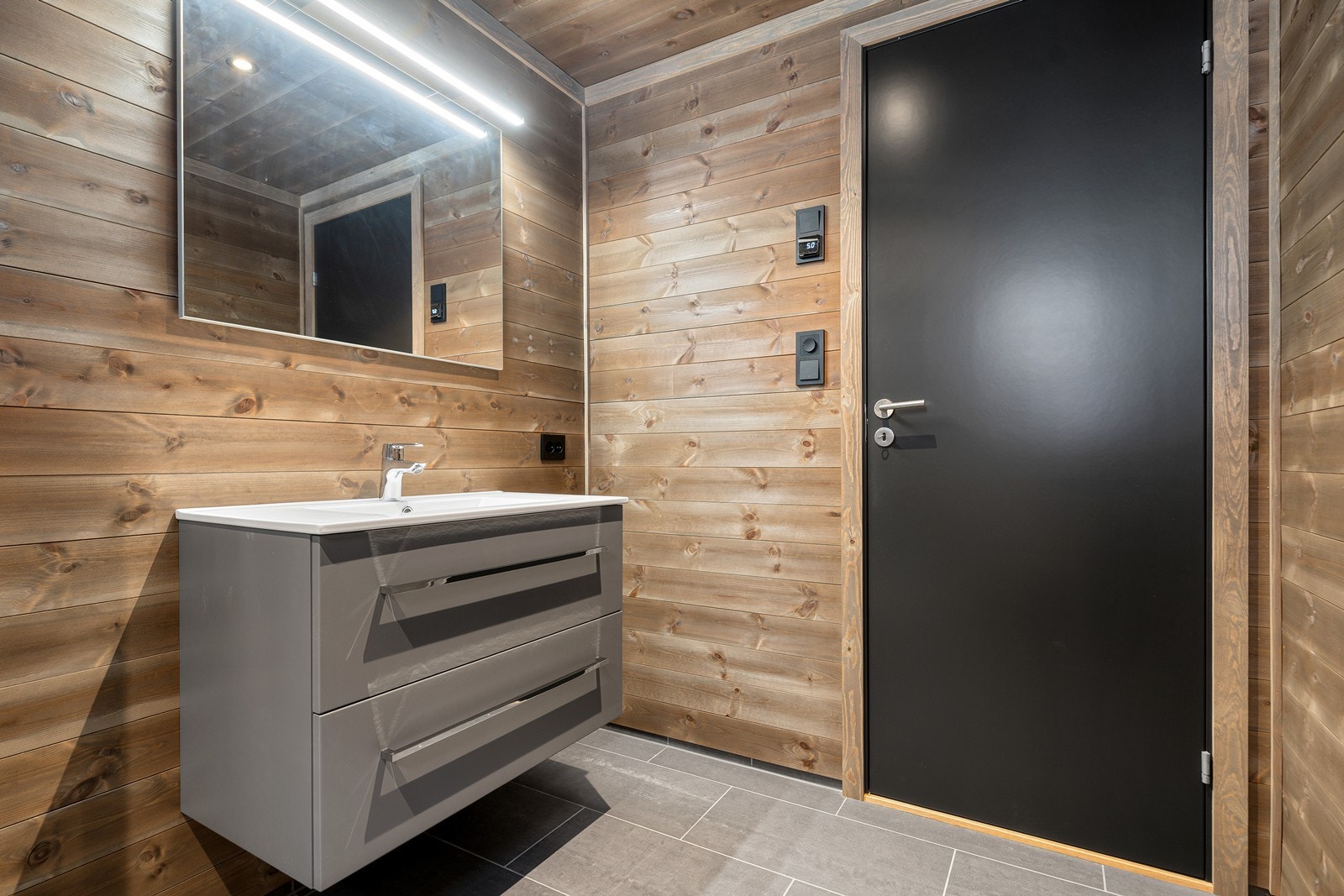 Ellers er badet innredet med dusjkabinett, toalett, elektrisk avtrekksvifte og heldekkende servant i romslig baderomsinnredning Galleribilde