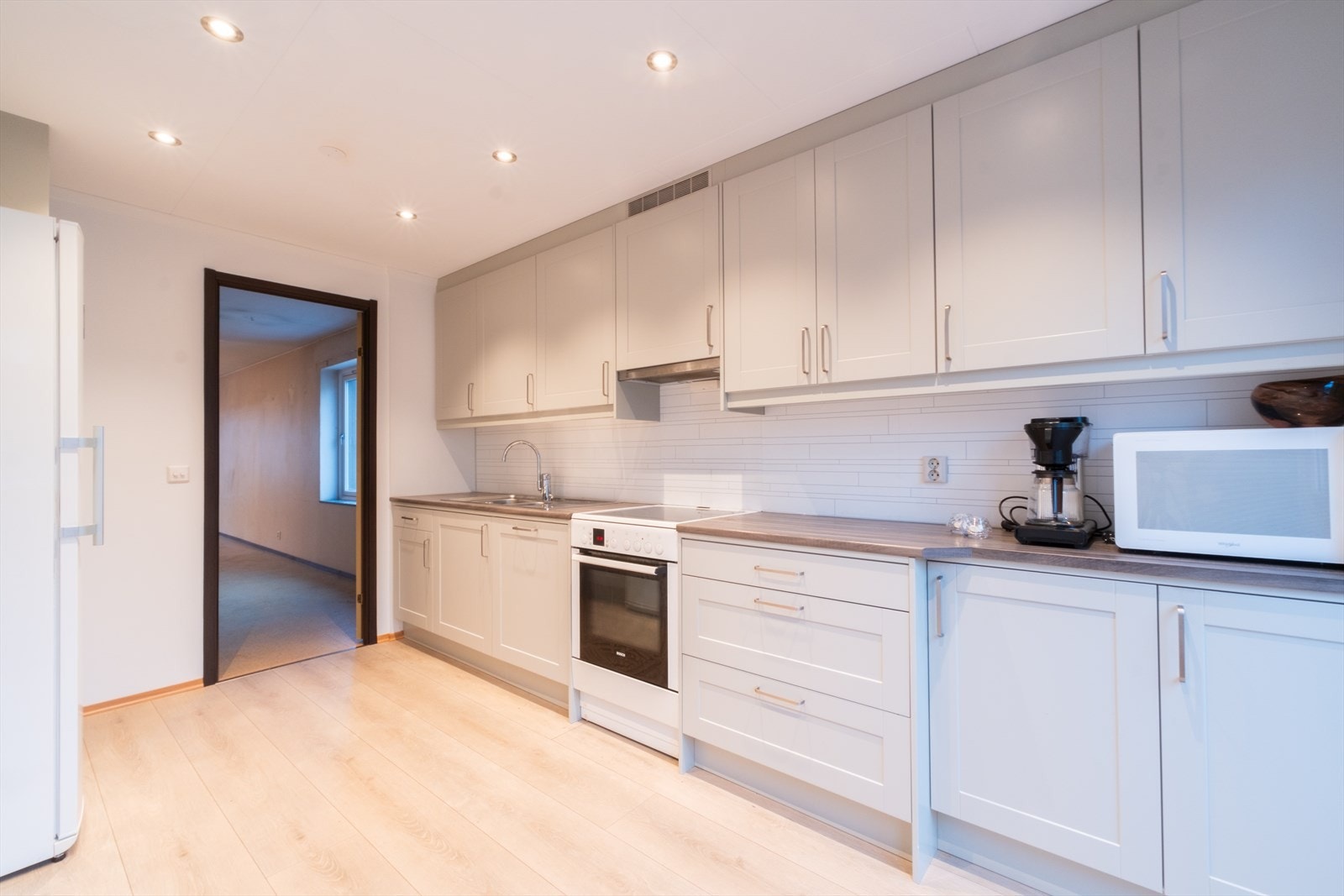 Innredning fra 2018 med glatte fronter, plater på vegg over kjøkkebenk og benkeplate i laminat. Galleribilde