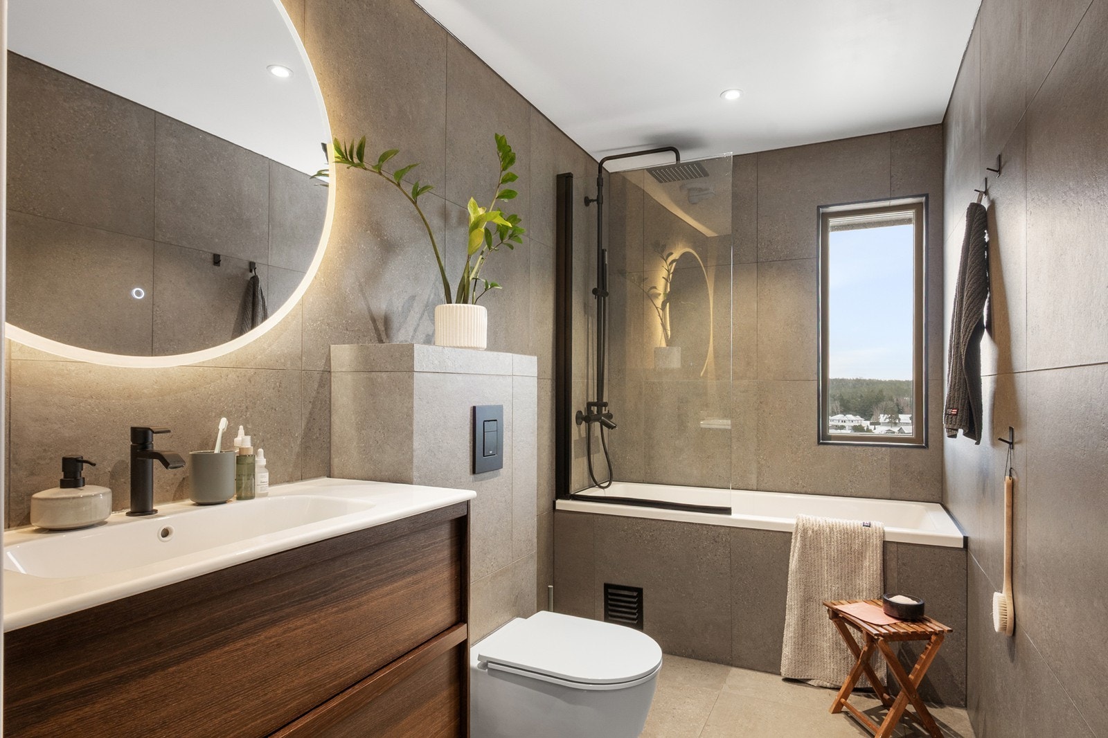 Innredningen består av badekar med dusjmulighet og glassvegg, vegghengt toalett og servantseksjon med skuffeinnredning. Servantområdet har speil med integrert belysning, og downlights i himlingen gir et behagelig lys Galleribilde