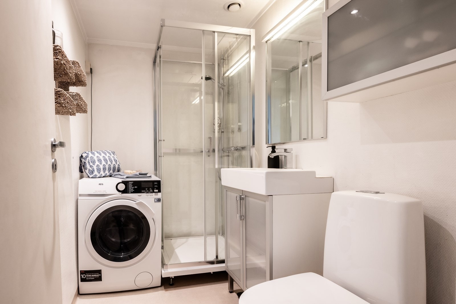 Bad innredet med dusjkabinett, gulvstående toalett og innredning med nedsunket servant med speil. Galleribilde