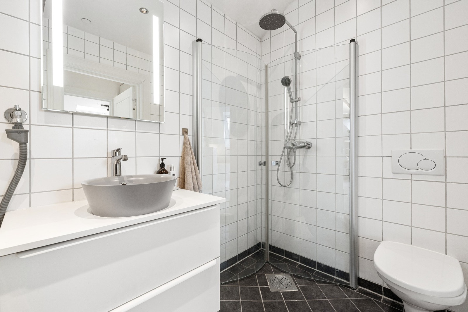 Stilren baderomsinnredning, speil med belysning og dusjhjørne med glassdører. Galleribilde