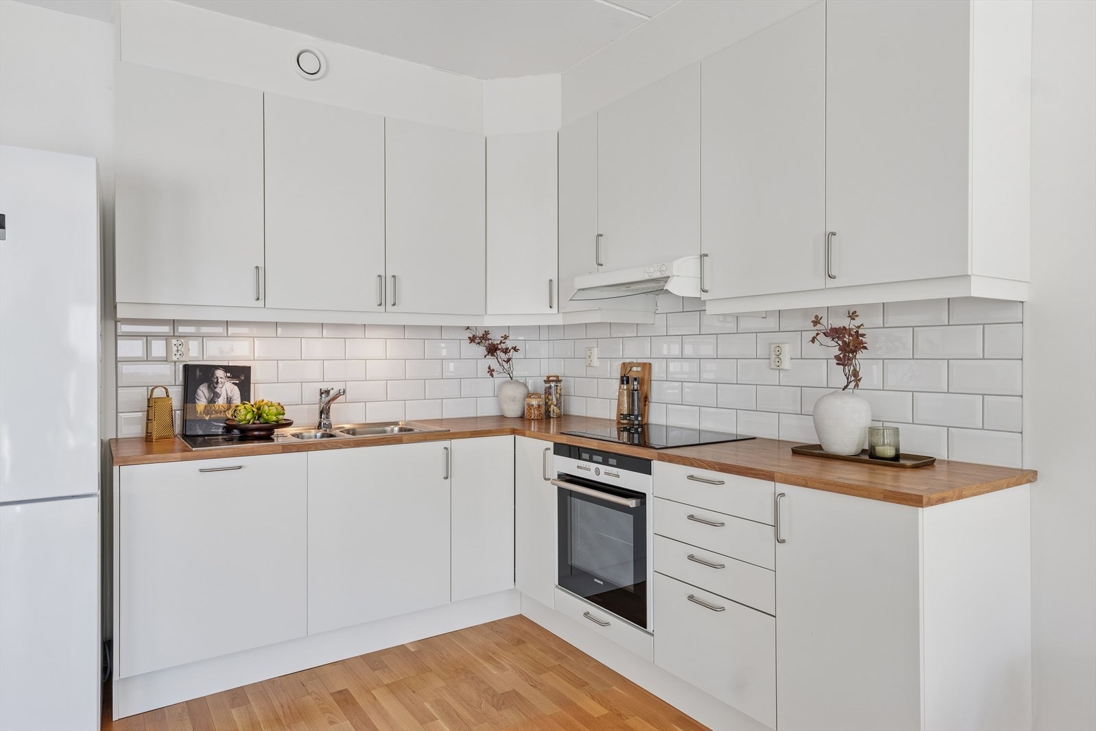 Funksjonelt kjøkken i hvit farge fra 2012 med takhøye skap, glatte fronter, stål håndtak og laminat benkeplate. Galleribilde