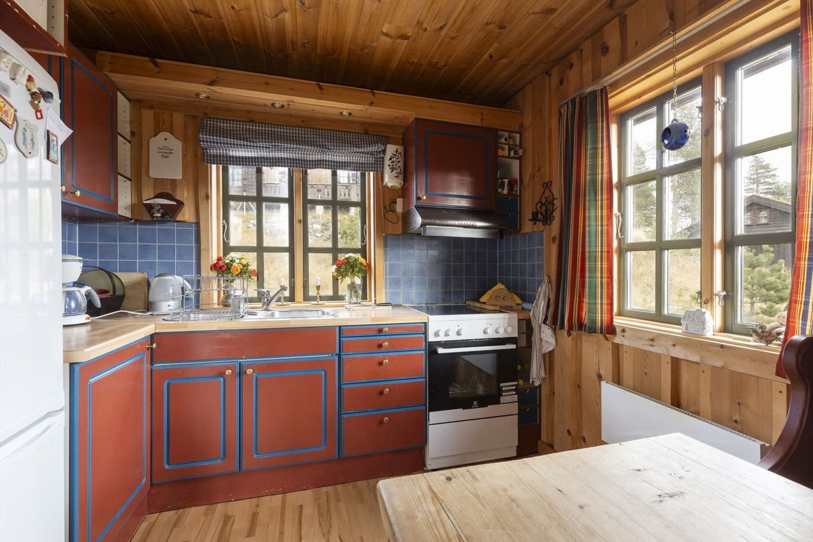 Kjøkkenet er innredet i en praktisk L-løsning med profilerte fronter, laminat benkeplater og fliser over arbeidsbenk. Det er opplegg for komfyr med ventilator, nedfelt oppvaskkum og plass til kjøleskap. Galleribilde