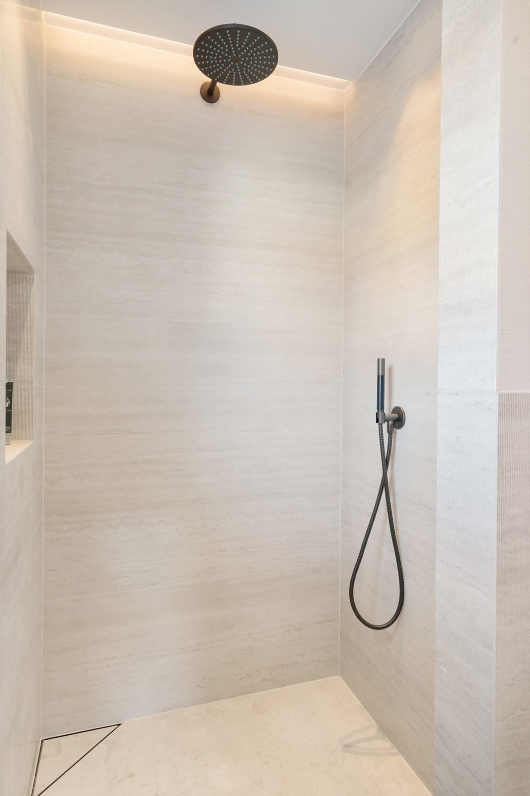 Dusjdør i glass, og innebygde dusjer med blandebatterier i bronse farge. Innfeldt belysning og nisje for dusjartikkler. Galleribilde