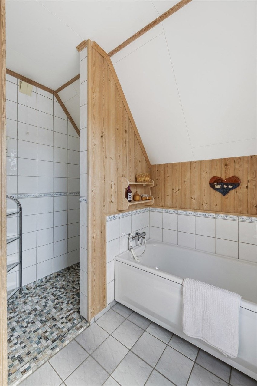 Badet har fliser på gulv og vegger, badekar, dusjhjørne med mosaikkfliser og panel på skråvegg. Galleribilde