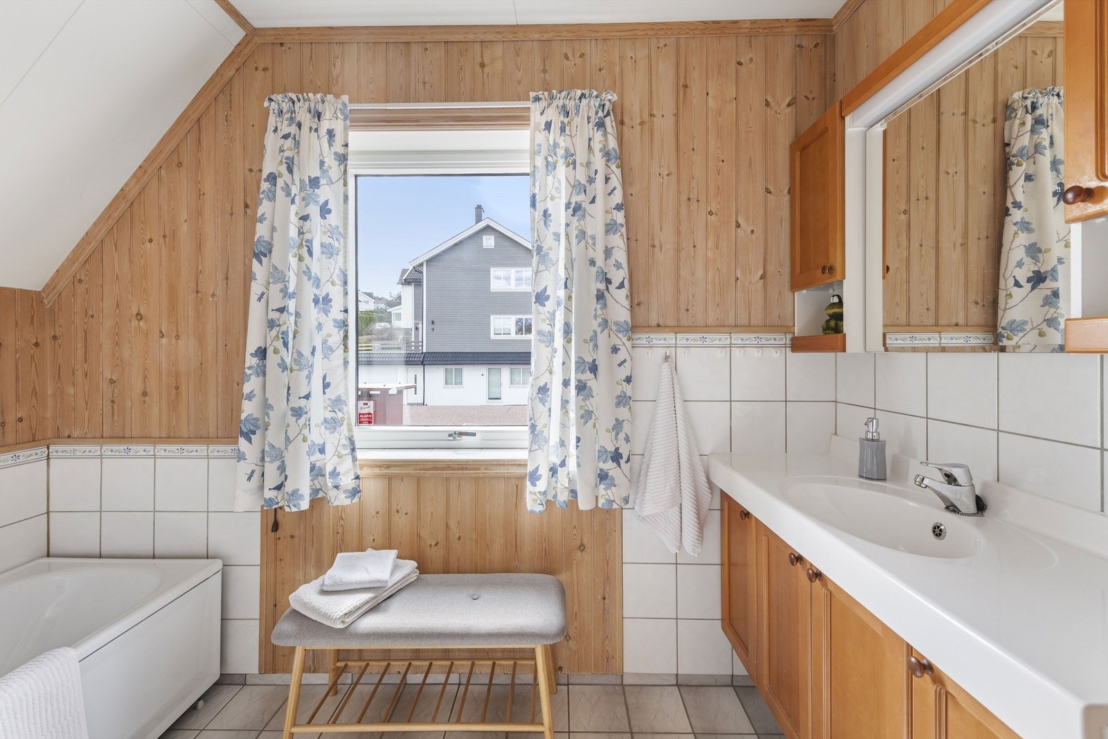 Bad med trepanel, fliser på vegg og gulv, samt et stort vindu som gir godt lysinnslipp. Galleribilde