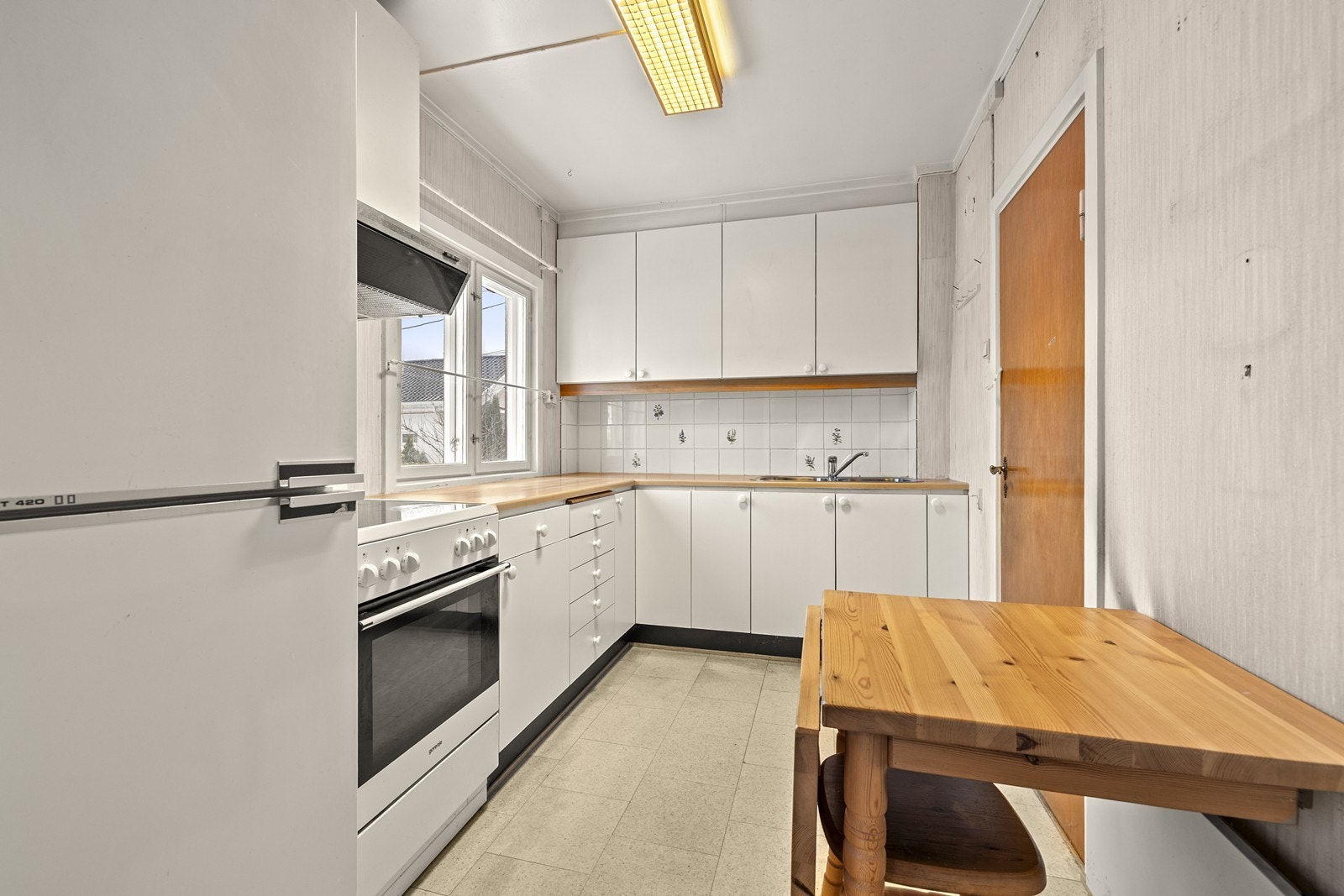 Lyst kjøkken med glatte fronter og laminert benkeplate, samt fliser på veggen over benken. Galleribilde