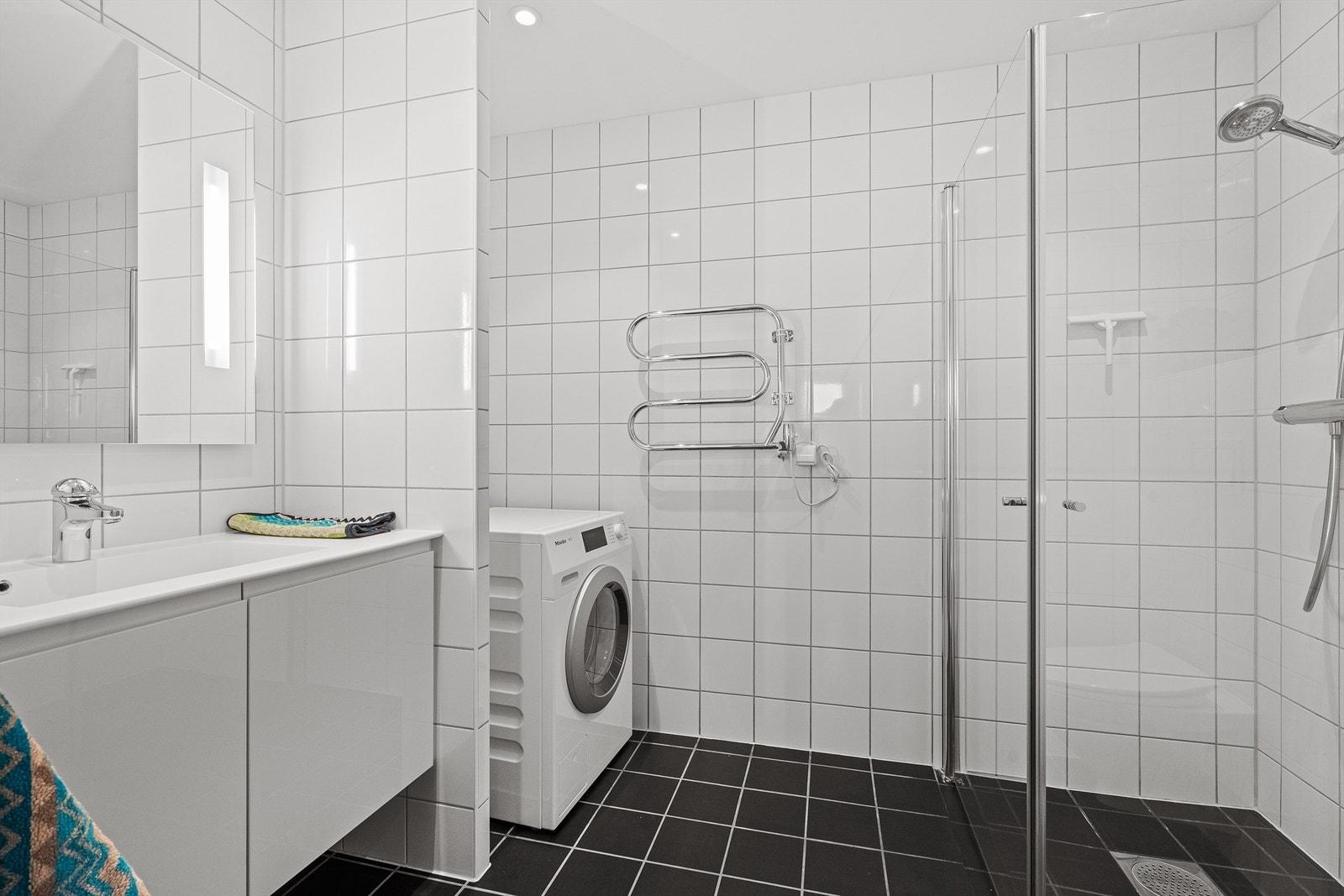 Fint helfliset bad av god størrelse med opplegg for vaskemaskin, samt plass til tørketrommel. Varme i gulv og servant med oppbevaring i skap. Stort speil på vegg. Håndkletørker på vegg. Galleribilde