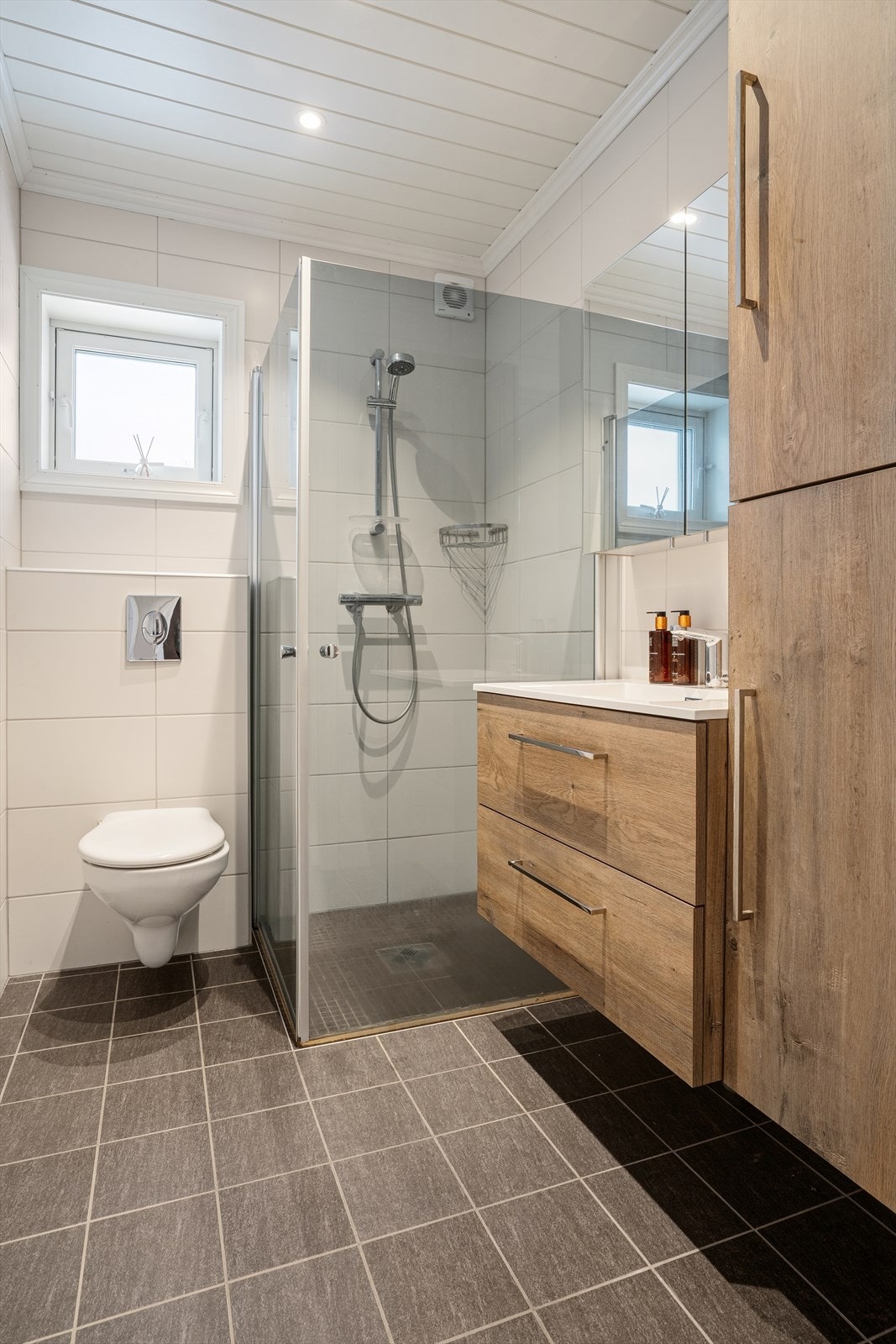 Badet ligger i byggets 1. etasje, opplyst fra 2022 og har fliser på vegger og gulv, med MDF-takplater og downlights. Det er trang adkomst til dusj. Galleribilde