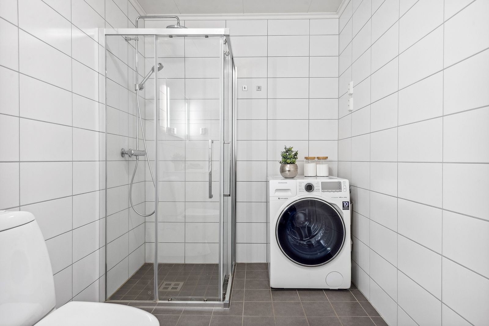 Dusjsone med skyvedører, gulvmontert toalett og opplegg for vaskemaskin. Galleribilde