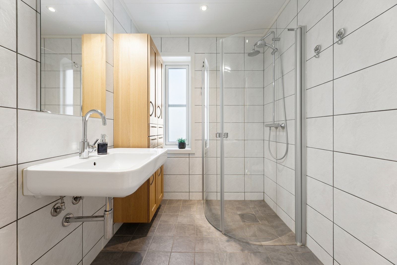 Lyst og delikat flislagt bad med dusjhjørne utstyrt med regndusjarmatur og hånddusj. Galleribilde