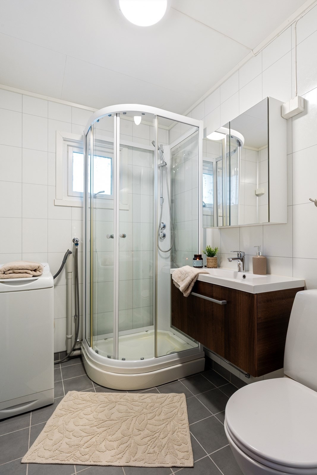 Pent bad med dusjkabinett, gulvstående toalett, opplegg for vaskemaskin og moderne baderomsinnredning. Varmekabler i gulv. Galleribilde