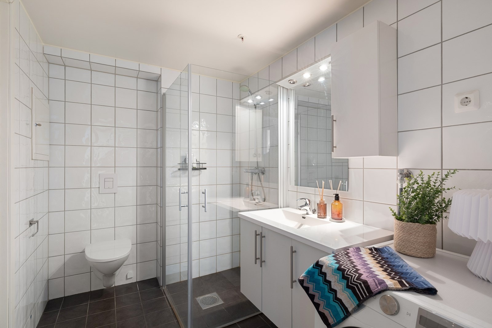 Flislagt bad med varmekabler i gulv, dusjhjørne, vegghengt toalett og moderne innredning. Galleribilde