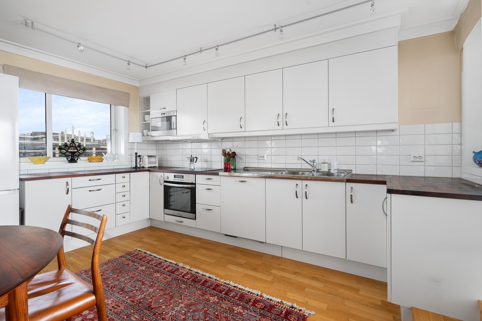 Flis på vegg over heltre benkeplate med gode arbeidsflater, nedfelt platetopp og heltrukket benkebeslag i rustfritt stål. Avsatt plass til frittstående kjøleskap. Galleribilde