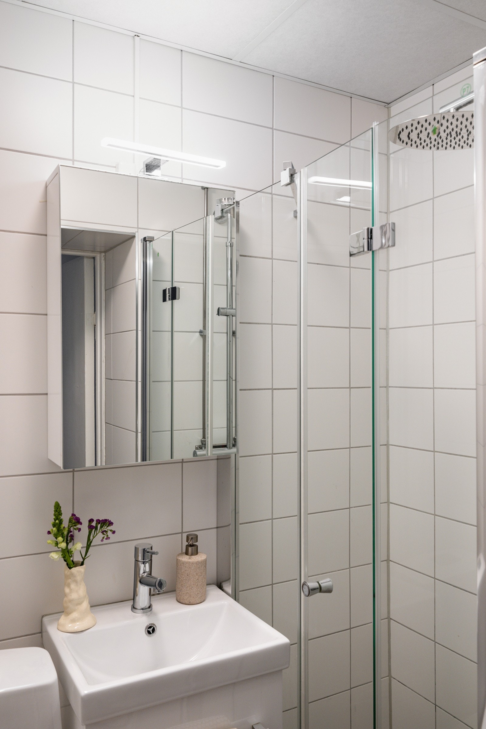 Lys baderomsinnredning med skuffer og ovenpåliggende servant, speilskap med belysning over. Galleribilde