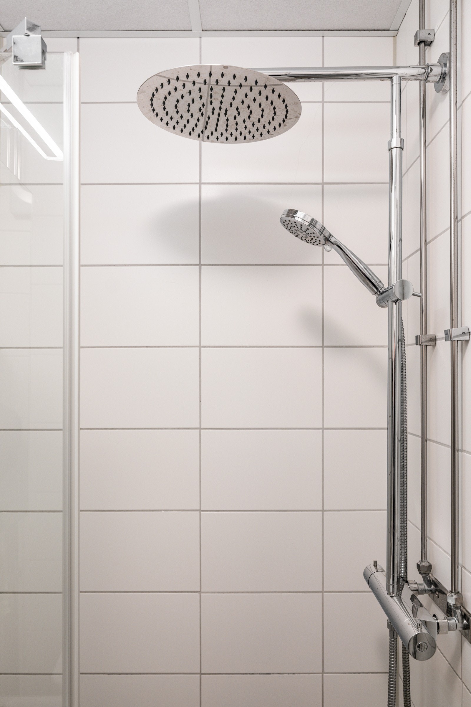 Dusjnisje med innfellbar glassdør og vegghengt armatur med både hånd- og regnfallsdusj. Galleribilde