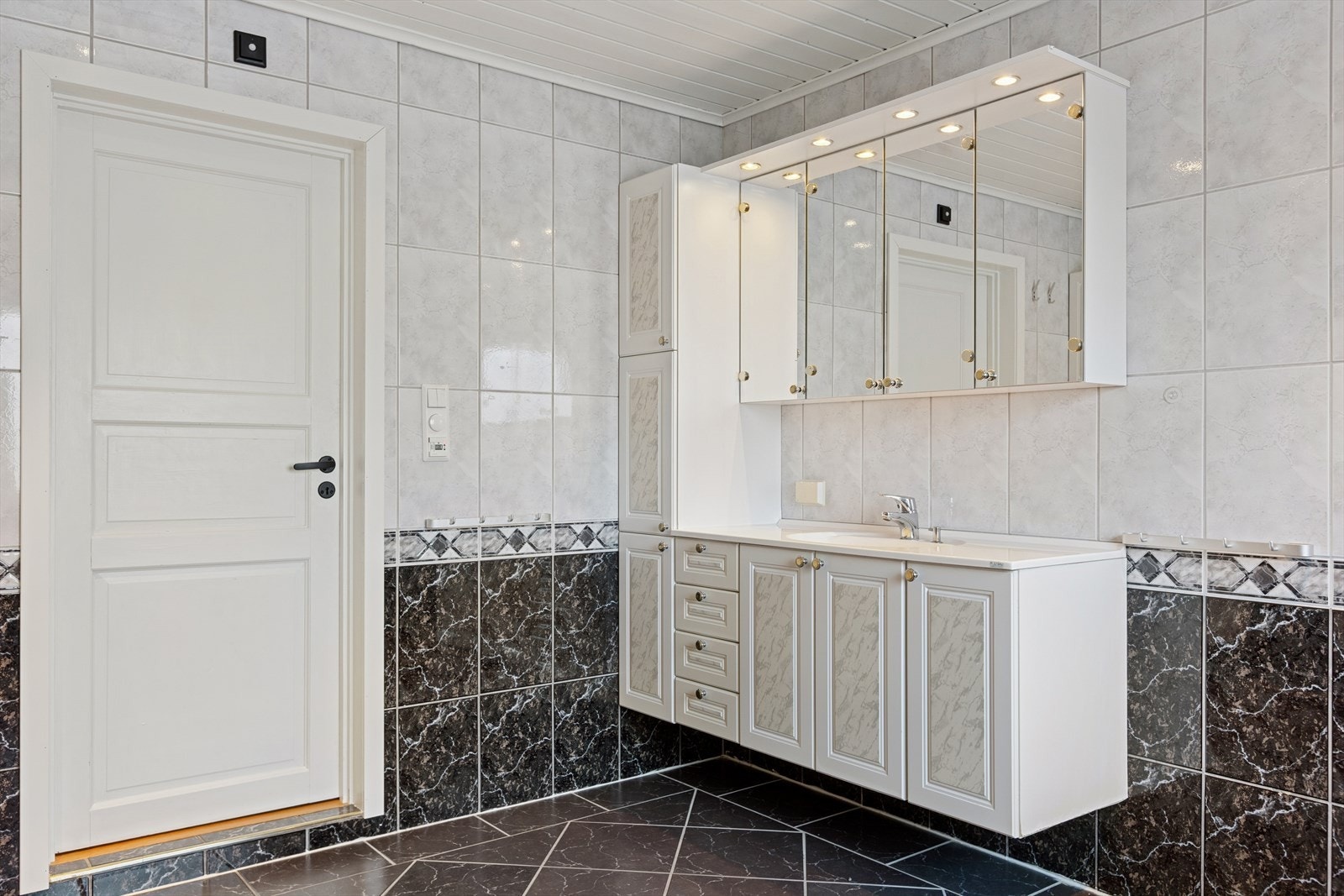 Baderommet er utstyrt med vegghengt toalett, moderne servantløsning med god benkeplass og baderomsinnredning, samt en praktisk dusjalkove med dør for effektiv skjerming av våtsonen. Galleribilde