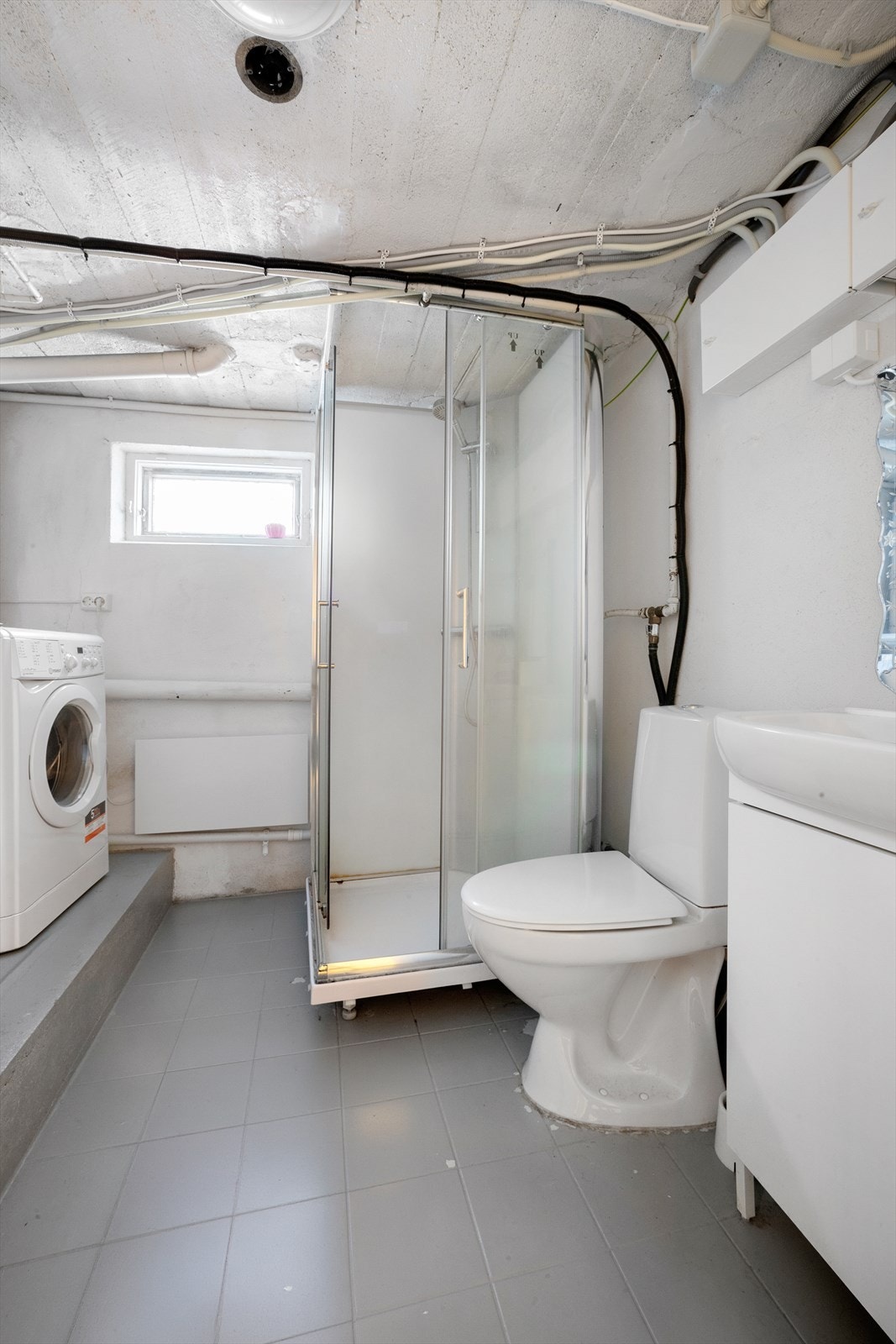 Bad/vaskerom med heldekkende servant, dusjkabinett, gulvmontert toalett og opplegg for vaskemaskin Galleribilde
