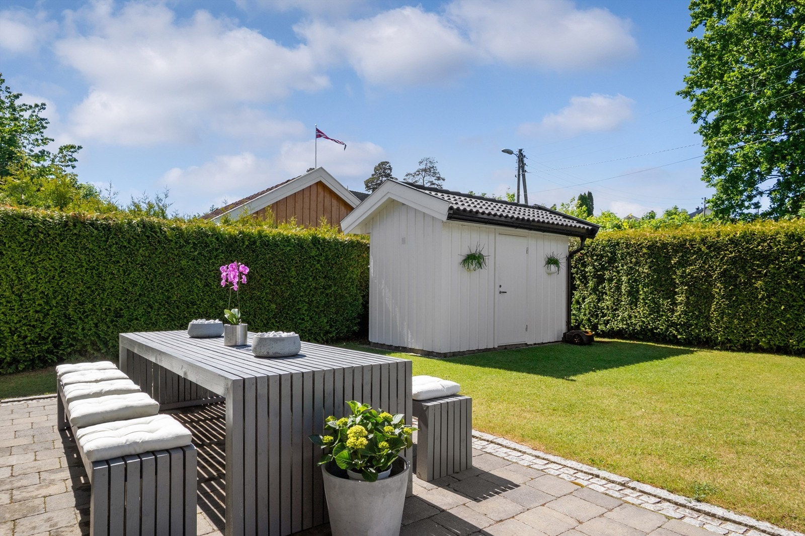 Hagen fremstår nærmest strøken med flere velplasserte prydbusker og levegger med plantekasser på siden mot nordvest. Galleribilde