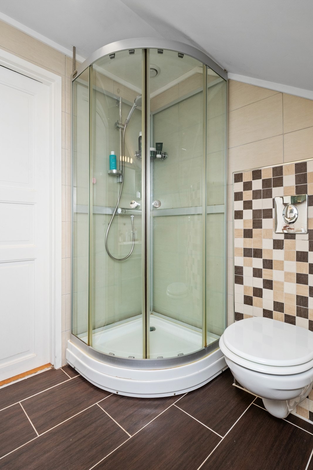 Innredningen består av en heldekkende servant på brun skuffeseksjon, matchende speilhylle, et veggmontert toalett og praktisk dusjkabinett. Galleribilde