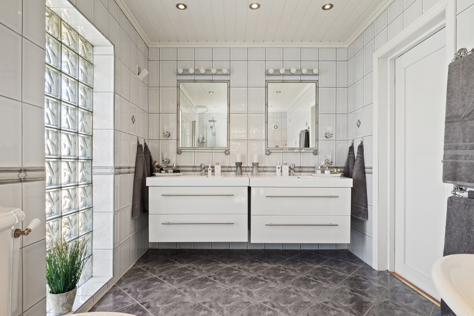 Videre er det et toalett i retrodesign, to servanter på hver sin hvite skuffeseksjon og to fastflisede speil med overlys. Galleribilde